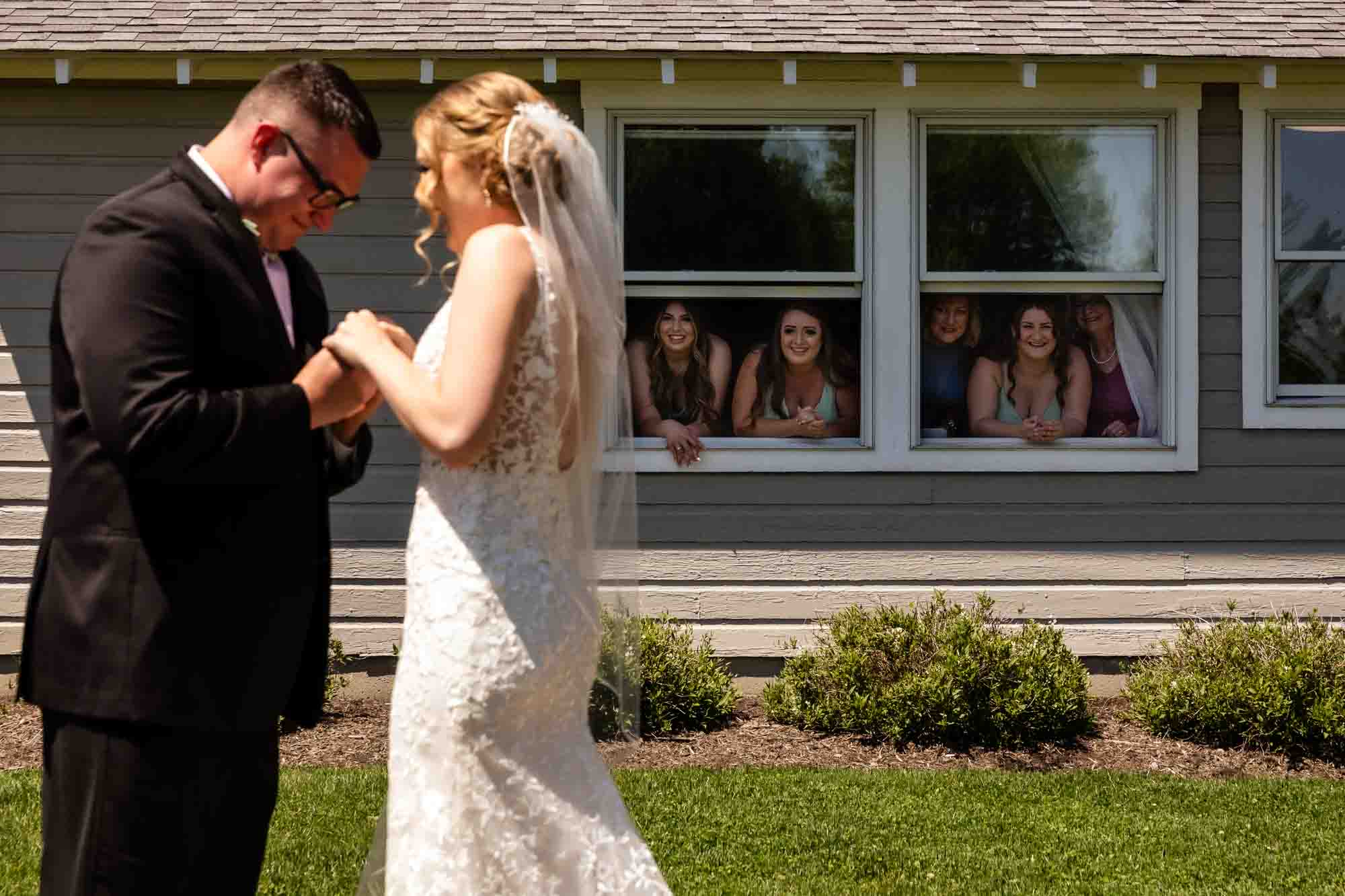 bridesmaids watch from a window as a bride and groom have their first look in a field at pinehall at eisler farms